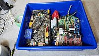 Blue bin with multiple computer circuit boards and accessories packed inside. Boards include several PCI cards with visible chips and ports.