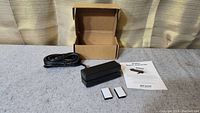 Photo of the MiniMag Magnetic Stripe Reader, USB cable, cardboard box, two white adhesive labels, and user manual arranged on a surface.