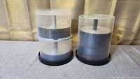 Three stacks of blank DVDs in clear plastic spindle cases with black bases, arranged on a cloth surface.