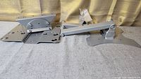 Two silver metal TV wall mount brackets, each with multiple mounting holes and adjustable arm on right.