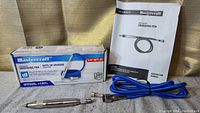 Mastercraft branded box, air powered engraving pen, and instruction manual arranged on cloth background.