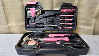 Opened tool kit showing hammer, tape measure, scissors, utility knife, hex keys, screwdriver handle, and screwdriver bits arranged in black molded case.