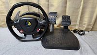 Thrustmaster Ferrari 458 racing wheel and pedal set with steering wheel showing buttons and paddle shifters alongside pedal set on floor, wired and untested condition.