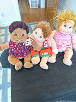 Photo showing three TY Beanie Kids dolls (Cutie, Buzz, Precious) seated on a black surface with original tags attached.