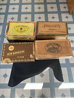 All four vintage cigar boxes shown together on a tiled floor: King Edward colorful box, Mata-Pura, Otto Boenicke and Schrader's Felix Brasil wooden boxes.