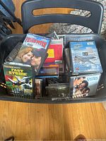 Plastic laundry basket filled with CDs, DVDs, and video game cases visible from top view.