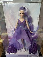 Front view of the Barbie doll in clear display case showing purple gown, tiara, and long lavender ponytail hair.