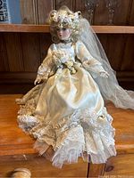 Front view of the 35-inch vintage porcelain wedding bride doll on a wooden surface with its floral veil and detailed dress