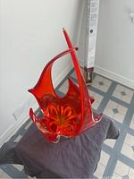 Full view of the bright orange sculptural glass art piece highlighting the flowing design and color.