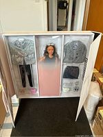 Opened packaging showing Barbie style curvy doll with multiple outfit pieces including jackets, skirts, shoes, and accessories.