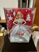 Front view of the 2021 Blonde Holiday Barbie doll in its original packaging with holiday silver glitter decorations on red background.