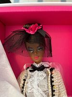 Close-up of Barbie doll face and upper body showing black veil with bright pink floral accent, lace blouse, tweed jacket with black trim and gold detailing.