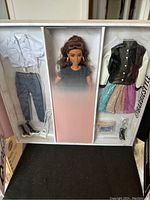 Front photo of the Barbie doll and accompanying outfits and accessories inside original packaging showing the doll in the center with two outfit sections on sides.