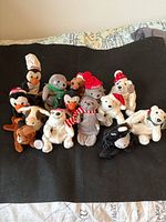 14 vintage Coca Cola Beanie Babies placed on black fabric, showing whole collection including bears, penguins, a dog, and others.