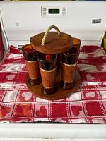 Front view of six amber tinted tiki glasses with teak wood wrappers inside round teak wood holder with rope handle