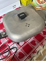 Top view of vintage Sunbeam frying pan with lid on red and white heart pattern tablecloth.