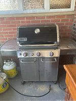 Front view of Weber gas grill on cart with closed black hood, two propane tanks beneath side shelf