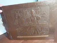 Close-up of the dark brown embossed cover of the 1920s photo album showing central female figure and surrounding Art Deco scenes.