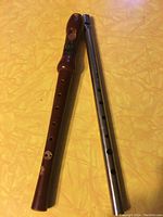 Wooden recorder and metal flute/whistle photographed side by side on a yellow surface.