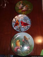 Top view of three 8-inch china plates each featuring different bird illustrations with natural background elements, showing overall condition and design details.