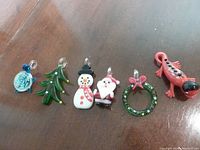 Photo of six lampwork glass ornaments and pendants displayed in a row on wood surface, showing detailed colors and loops for hanging.