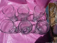 Top-down view of the six Coca-Cola glasses arranged in a circle, showing clear textured glass and embossed logos.