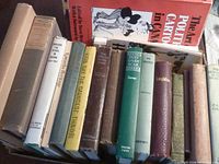 Photo showing a row of assorted older books with titles visible on spines including political cartoons, and various literary works.
