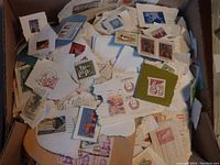 Box containing numerous torn pieces of envelope paper with attached Canadian and world postage stamps in various colors and designs.