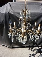 Metal chandelier with ornate metal arms, candle styled bulb holders, and hanging glass crystals shown from front angle.