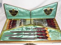 Open display box showing six matching serrated edge knives and six forks with gradient brown and tan handles, plus carving utensils.