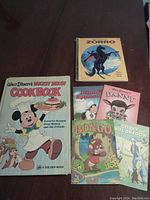 Six vintage Disney children's books laid out on a table including Mickey Mouse Cookbook, Zorro, Johnny Appleseed, Danny, Bongo, and Corky and White Shadow.