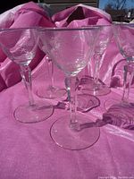 Five clear wine glasses arranged on pink fabric with visible etched starburst comet pattern on bowls and faceted geometric stems.