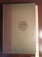 Full closed book showing front cover and cloth binding along with measurement ruler for size estimation.