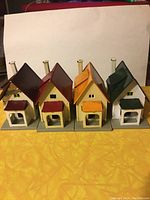 Front view of four HO scale metal houses with varying roof colors: dark red, red, orange, and green.