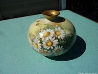 Bulbous hand painted Limoges vase with bright white daisies and green leaves on yellow background, viewed standing upright.