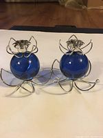Pair of blue lucite globe candle holders with silver metal wire floral petal designs at base and candle cups.