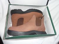 Side view of tan men's slip-on boots with black sole inside box, showing elastic side panels.