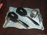Silver-toned mirror tray with metal handles, vintage hand mirror and brush set with black backing and silver detail, small glass dish with metal lid and red knob