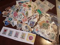 Overview of a large, mixed lot of mostly Canadian used stamps spread out on a table with some stamps in small plastic bags and a collection of Bulgarian floral stamps laid out on a card.