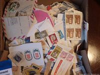 Box filled with loose used Canadian postage stamps attached to torn envelope pieces and paper fragments showing multiple stamp designs and colors.