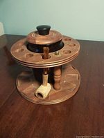 Photo of wooden circular pipe stand with multiple pipe holes and a corn cob pipe inserted.
