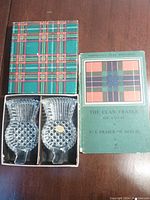 Pair of thistle-shaped glass dishes in a presentation box with tartan-patterned lid, and a Scottish clans book with tartan design on the cover.
