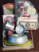Top view of lot showing boxed puzzle, bags of game pieces and play money, and metal toy items resembling kitchenware.