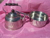 Photo of stainless steel kettle and pot set on a pink background, showing both items in full view.