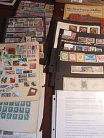 Photo showing multiple stock pages containing various new and used postage stamps, some loose stamps, and a beginners' stamp album.