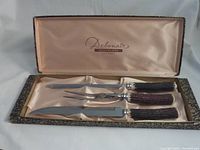 Full view of the carving set in satin-lined presentation box showing three pieces: carving knife, carving fork, and sharpening steel with horn-effect handles.