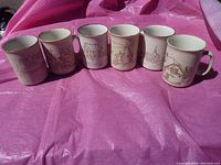 Photo of 6 vintage mugs featuring line drawings of historical buildings. Mugs displayed side by side on a pink surface.
