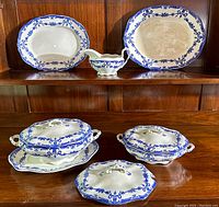 Display of two platters, gravy boat, covered vegetable dish, and two tureens with lids on a wood shelf.