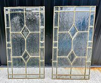 Pair of antique leaded glass windows with brass metal framing, front view showing geometric diamond and rectangular pattern and textured glass panels.