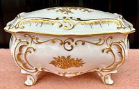 Front and side view of vintage white porcelain vanity box with gold floral design and gilded trim on four feet